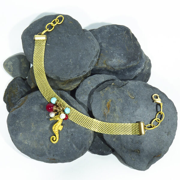 Pulsera artesanal con cadena plana dorado mate con caballito y piedras en rojos y turquesas.